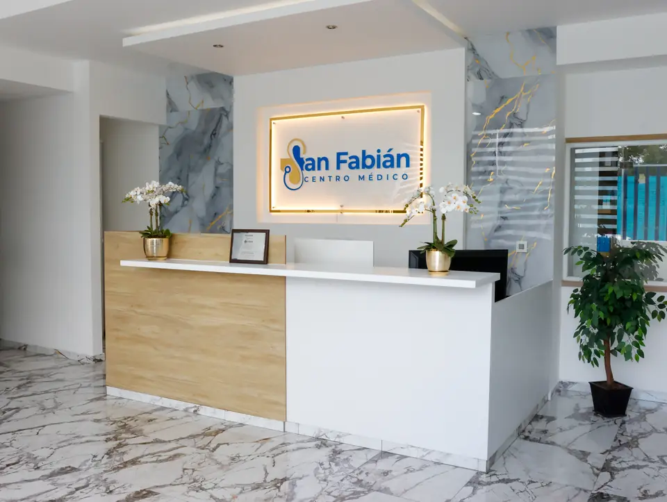 Recepción de Centro Médico San Fabián con el logotipo iluminado, mármol con vetas doradas y orquídeas blancas